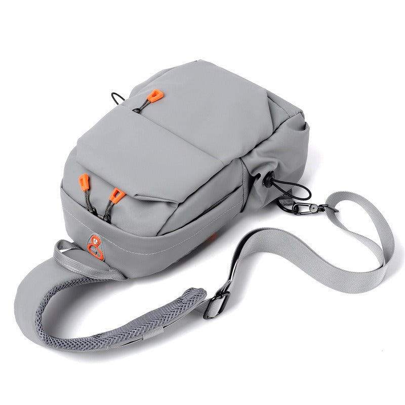 Gray crossbody sling backpack bag, side view with orange zipper pulls and fabric web strap