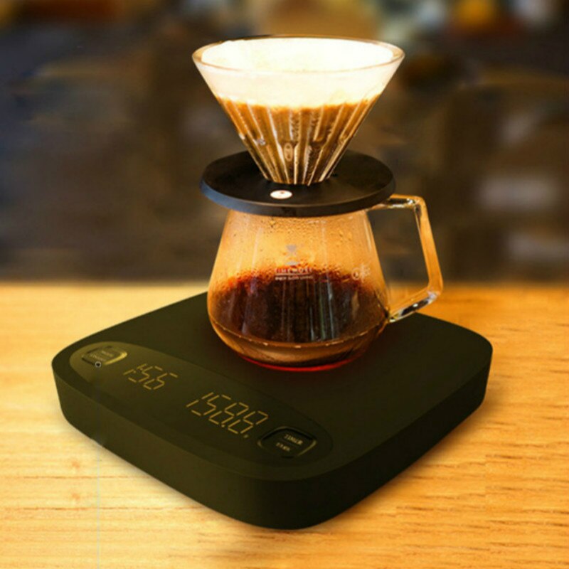 Black coffee electronic scale on a wood table supporting a pour-over carafe