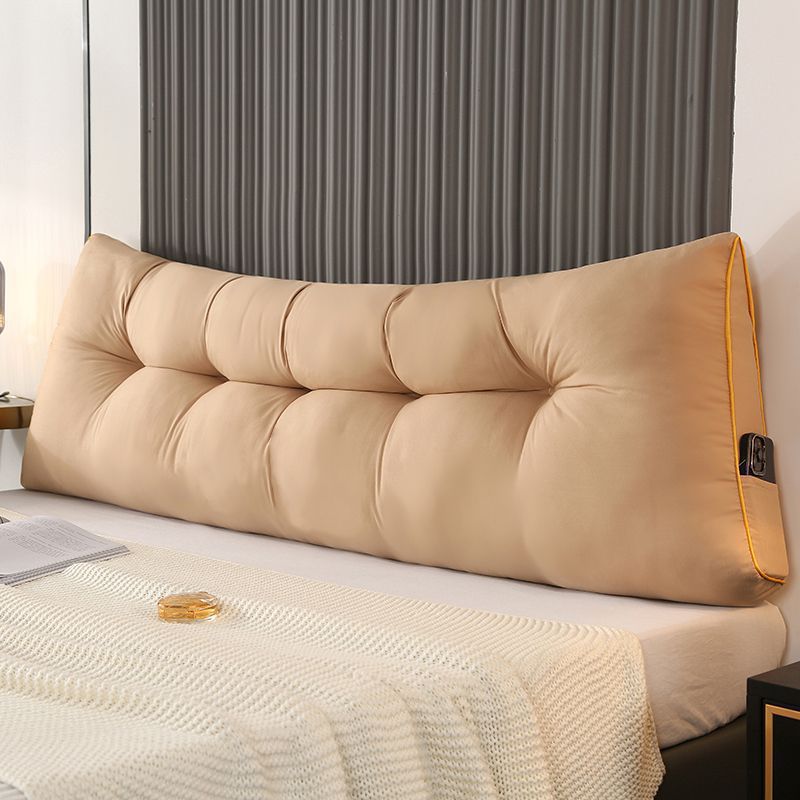 Beige triangular tufted bed backrest cushion with orange piping and side pocket.