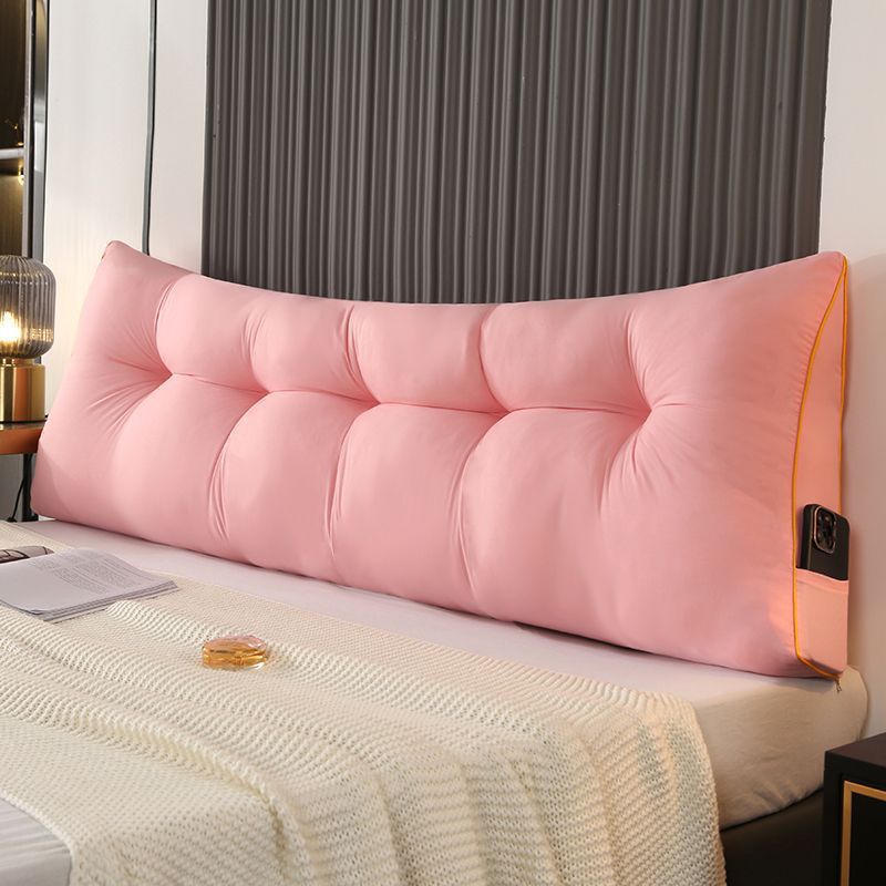 Dark gray triangular tufted bed backrest cushion with orange piping and side pocket.