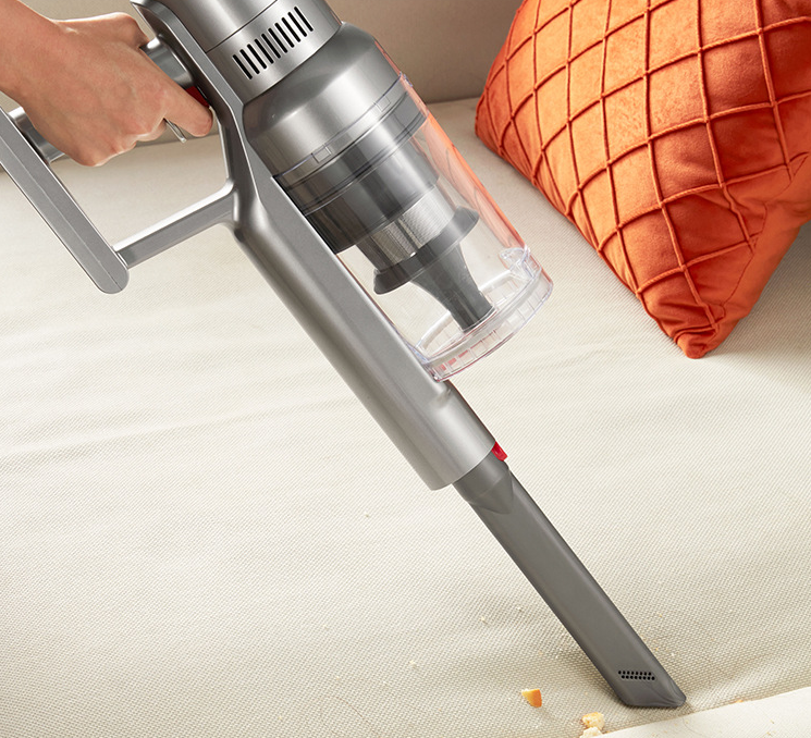Cordless vacuum cleaner cleaning upholstery, silver body and transparent dust container