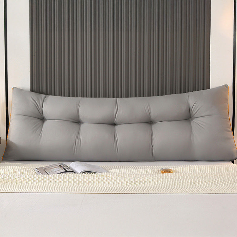 Gray triangular tufted bed backrest cushion with orange piping, set on the bed.