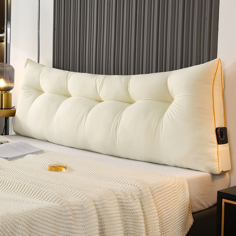 Cream triangular tufted bed backrest cushion with orange piping and side pocket.