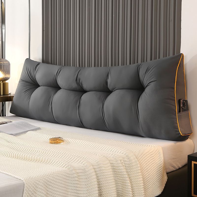 Dark gray triangular tufted bed backrest cushion with orange piping and side pocket.