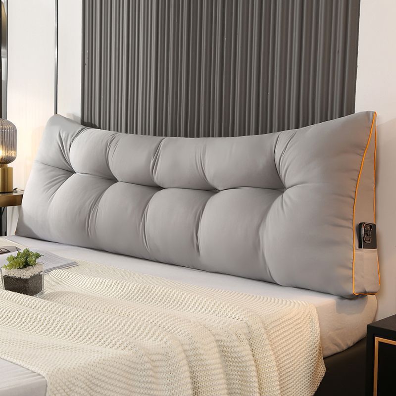 Light gray triangular tufted bed backrest cushion with orange piping and side pocket.