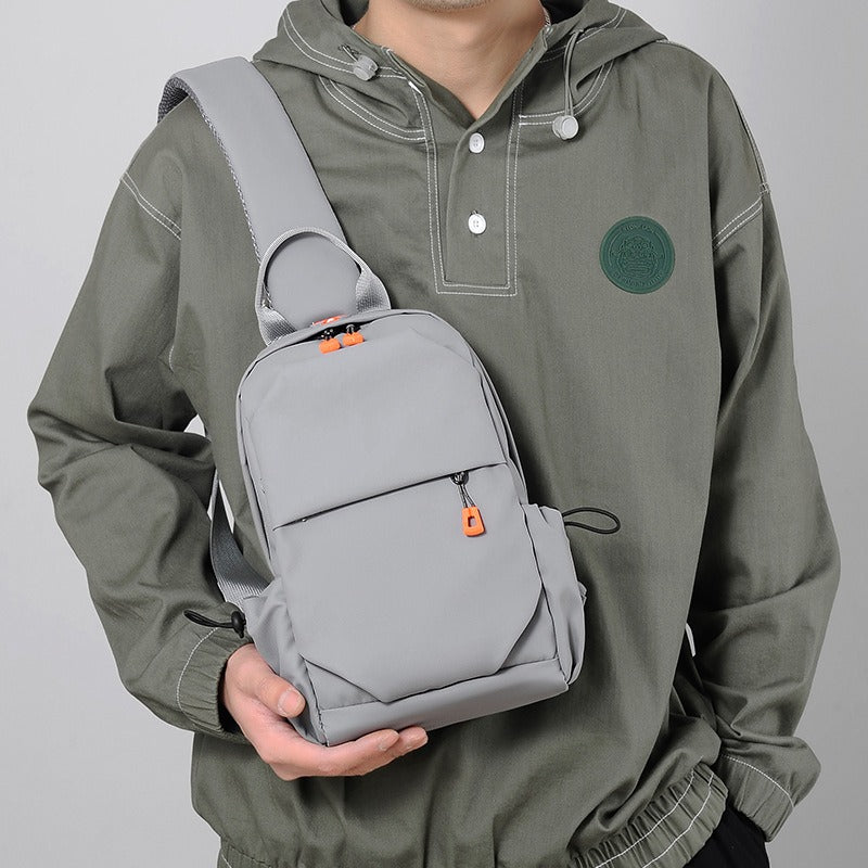Gray crossbody sling backpack bag with orange zipper pulls, worn on the front