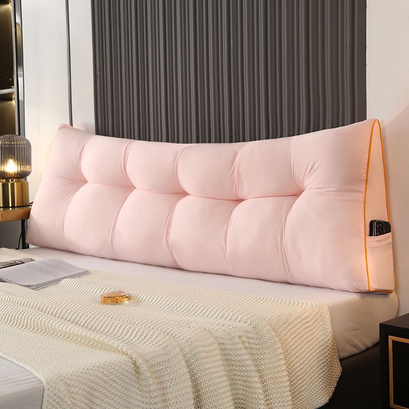 Pale pink triangular tufted bed backrest cushion with orange piping and side pocket.