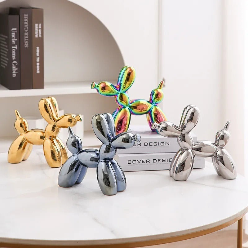 Iridescent rainbow balloon dog figurine with gold and silver figures nearby