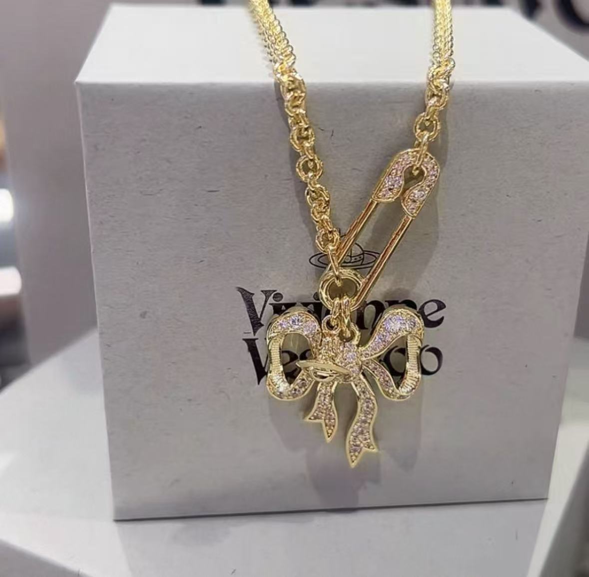 Gold-tone chain necklace with bow pendant charm on gift box