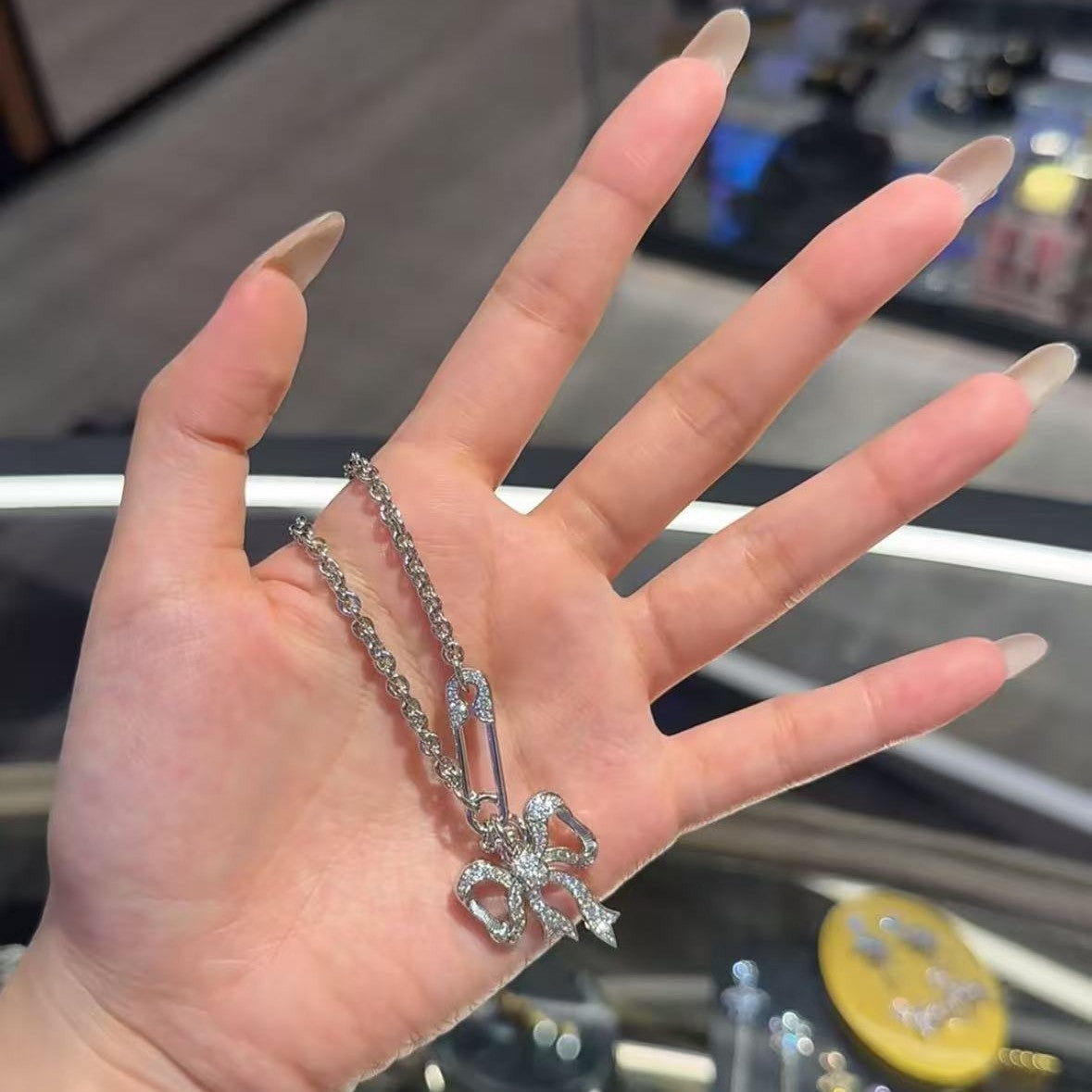 Silver chain necklace with bow pendant charm on open palm