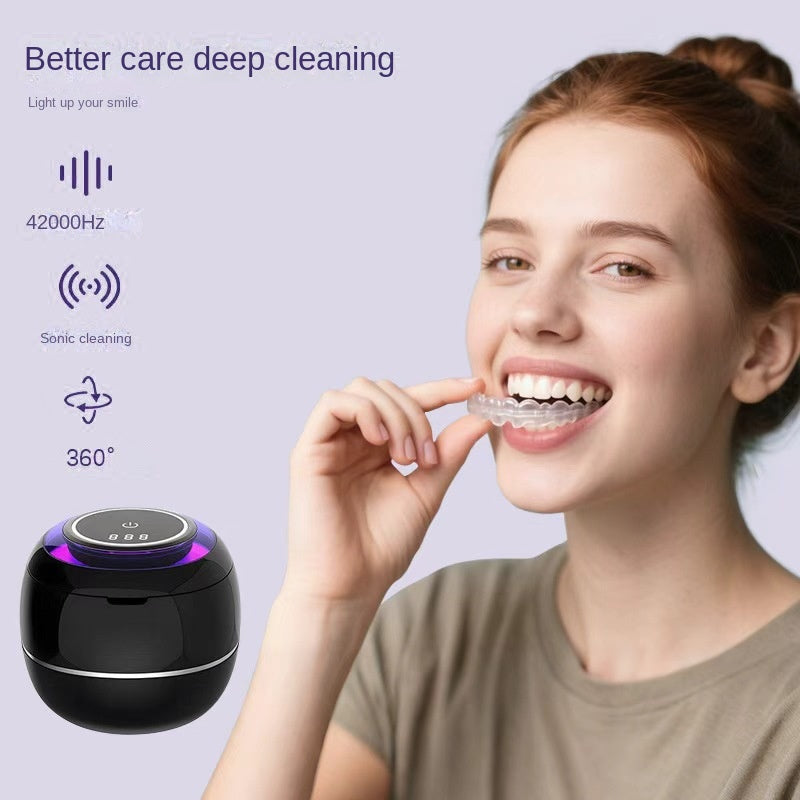 Ultrasonic denture cleaner in black with purple glow ring while holding a clear tray